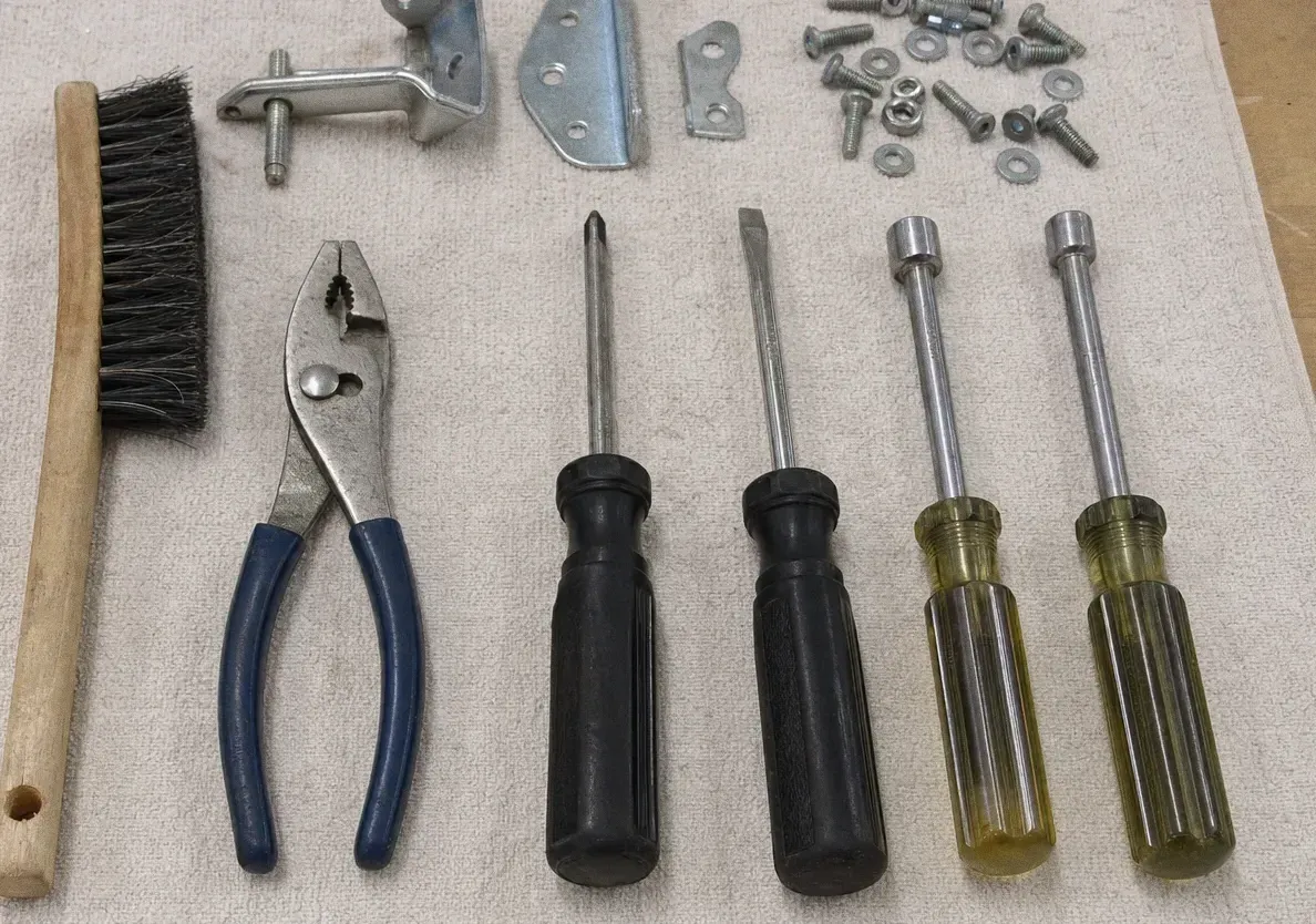 Slip-joint pliers, black-handled screwdrivers, yellow nut drivers and a wire brush laid out on a canvas cloth