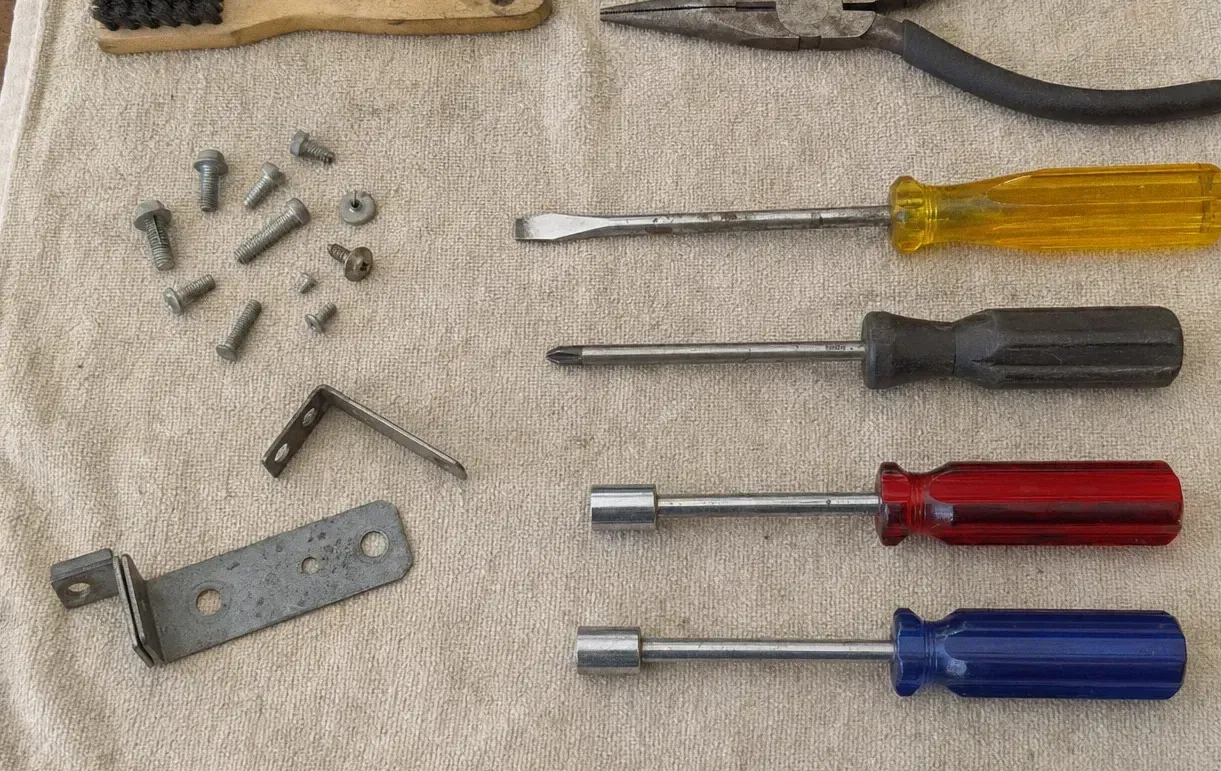 Bolts, washers, a hex key, an angle bracket and a flat steel plate laid out beside four coloured screwdrivers